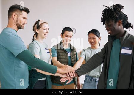 Waist up portrait of international volunteers team stacking hands in unity and support Stock Photo
