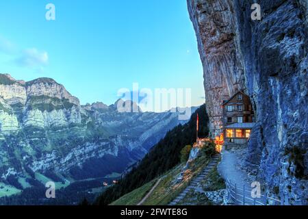 After sunset view of the magical Aescher Cliff (Appenzell Canton, Switzerland) and the moutain restaurant catering to hikers. A crescent moon is visib Stock Photo