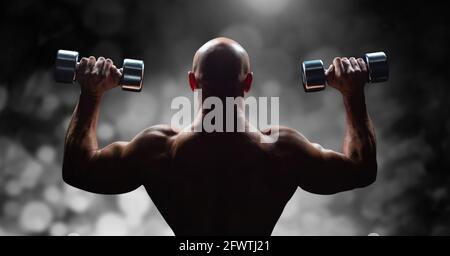 Composition of rear view of muscular bald man exercising with dumbbells over black and white blur Stock Photo