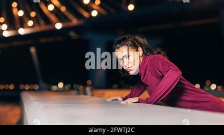 Sportswoman doing push-ups near embankment at night Stock Photo