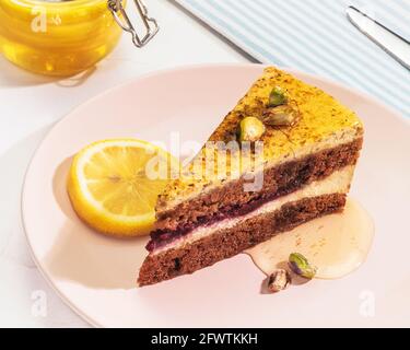 Horizontal morning food composition with a piece of pistachio lemon pie with honey and nuts on a pink plate with a jar of honey on a white background Stock Photo