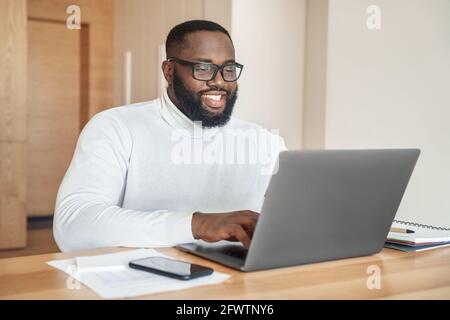 Happy smiling bearded african american man working typing on laptop keyboard Stock Photo