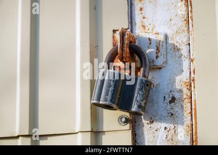 Closed padlock hanging on the hinges on a gray rusty iron door Stock Photo