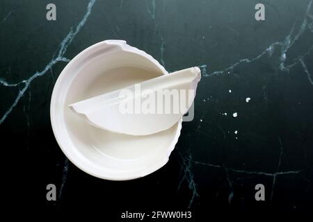 Broken white ceramic baking bowl with fragments on black marble floor Stock Photo