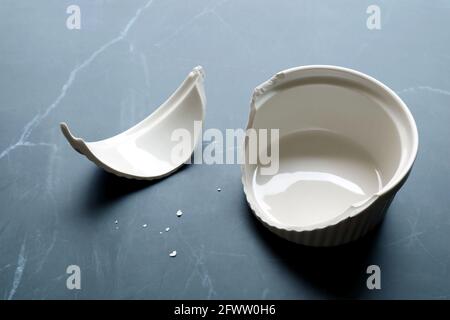 Broken white ceramic baking bowl with fragments on black marble kitchen counter top Stock Photo