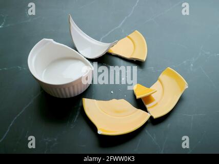 Broken white and yellow pottery scattered on black kitchen floor Stock Photo