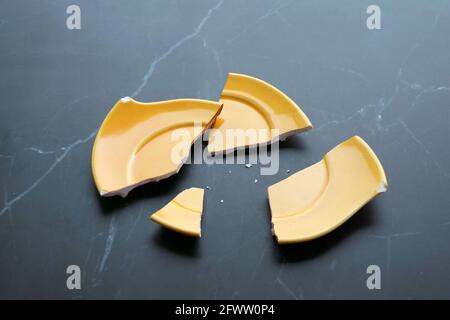 Broken Vivid Yellow Ceramic Saucer Scattered on Black Marble Kitchen Tabletop Stock Photo