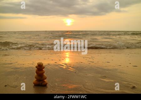 Closeup stack of balanced pebble stones on the sunset beach against splashing waves Stock Photo