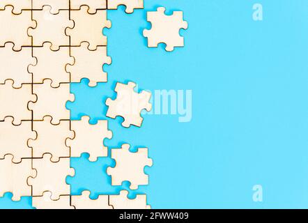 Putting together a wooden jigsaw puzzle on a blue paper background Stock Photo