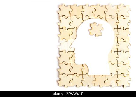 Human head shaped paper silhouette with a jigsaw piece on top of a wooden puzzle isolated on white Stock Photo