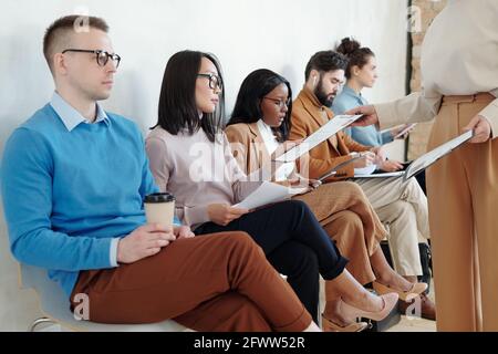 Recruiter giving questionnaire to multi-ethnic job applicants sitting in row and waiting for interview Stock Photo