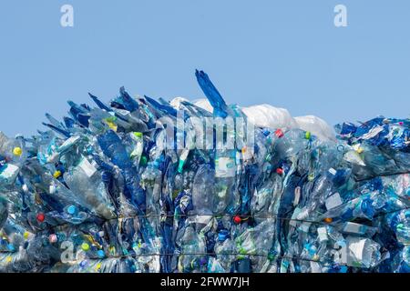 Pressed empty beverage packagings on blue sky background. Used recyclable PET bottles with colored caps in bale. Waste sorting, recycling or disposal. Stock Photo