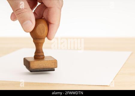 Hand holding a Rubber stamp and blank paper on wooden table. White background. Copy space Stock Photo