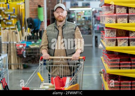 Happy middle aged man walking along displays in large modern hardware supermarket Stock Photo