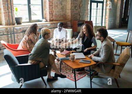 Two happy young businesswomen shaking hands among colleagues at business meeting Stock Photo