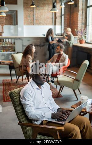 Serious African businessman using laptop against busy colleagues Stock Photo
