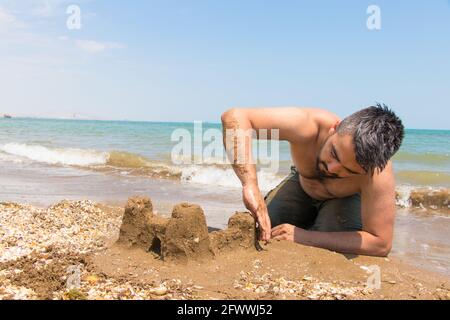 Time to make dreams come true. Man build a castle of sand on the beach. The concept of active life. Stock Photo