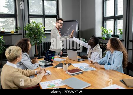 Successful coach giving high five to young African businessman after presentation Stock Photo