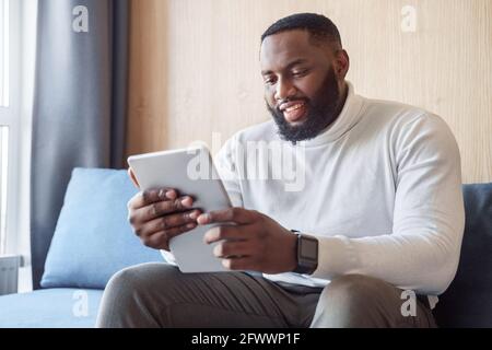 Smiling african american man holding digital tablet sitting on couch at home Stock Photo