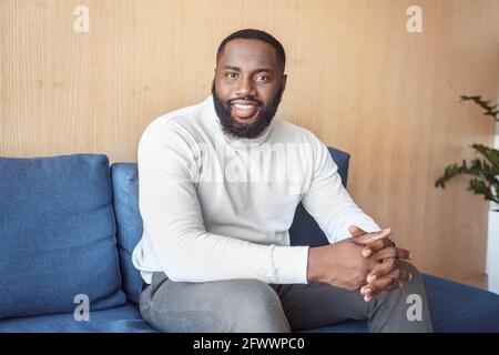 Trendy fashion african american guy with beard relaxing at home sitting on couch Stock Photo