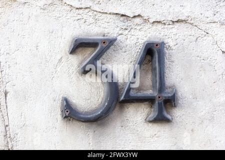 Number 34 (thirty four) in metal on a white plaster wall Stock Photo