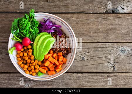 Healthy Buddha bowl with rapini, quinoa, sweet potato, chickpeas and avocado. Top view over a rustic wood background. Stock Photo