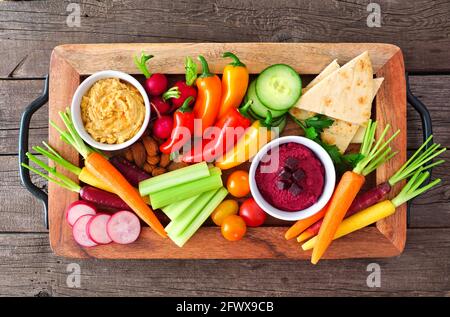 Variety of fresh vegetables and hummus dip on a serving tray. Above view on a rustic wood background. Stock Photo