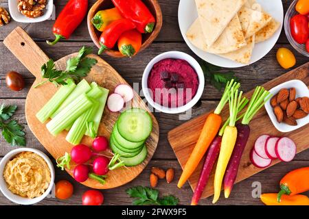 Table scene with a variety of fresh vegetables and hummus dips. Overhead view on a rustic wood background. Stock Photo