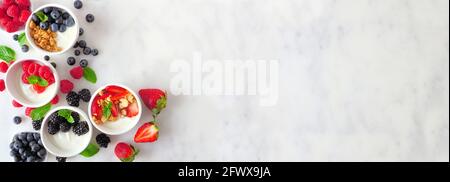 Healthy yogurt bowls with assorted berries and granola. Banner with corner border against a white marble background. Copy space. Stock Photo