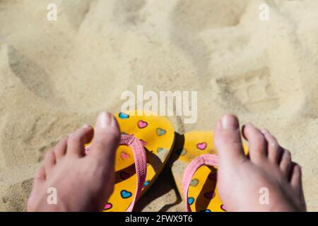 Defocus dirty bright yellow and pink slippers flip flops with hearts on the sand. Blurred female feat. Summer background.The concept of heat, relaxati Stock Photo