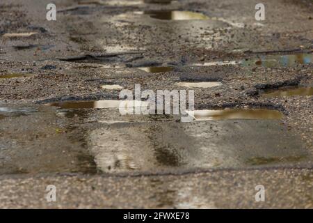 potholes and puddles on bad broken wet asphalt road after rain - full frame background Stock Photo