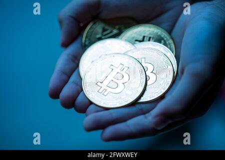 Shiny silver bitcoins in hand palm over dark blue background. Cryptocurrency market crash concept. Stock Photo