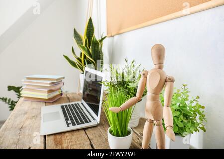 Books, laptop, wooden mannequin and houseplants on table in room Stock Photo