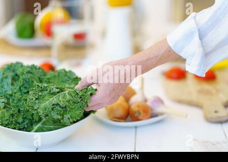 Cropped close up shot of retired woman in apron preparing fresh healthy vegetable salad while cooking food for whole family during retirement in modern kitchen at home, fresh organic vegetables Stock Photo
