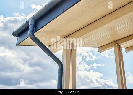 Contemporary grey metal rainwater downpipe installed on roof of new building with wooden terrace on cloudy day close view Stock Photo