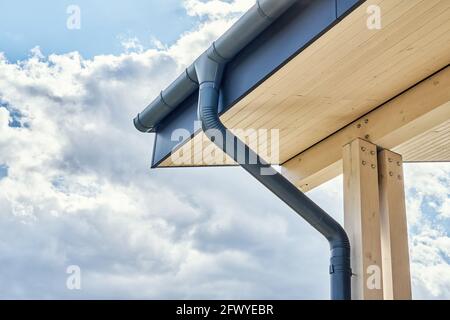 Contemporary grey metal rainwater downpipe installed on roof of new building with wooden terrace on cloudy day close view Stock Photo