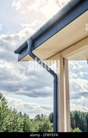 Contemporary grey metal rainwater downpipe installed on roof of new building with wooden terrace on cloudy day close view Stock Photo