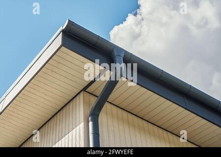 Contemporary grey metal rainwater downpipe installed on roof of new building on cloudy day close view Stock Photo