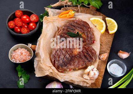 Delicious prepared meat steaks with seasoning and herbs on dark background. Geilled food concept. Stock Photo