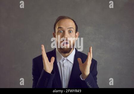 Shocked businessman entrepreneur in suit headshot portrait on grey background Stock Photo