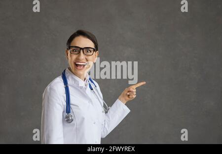 Funny crazy female doctor standing on gray background smiling with wide open mouth and eyes. Stock Photo