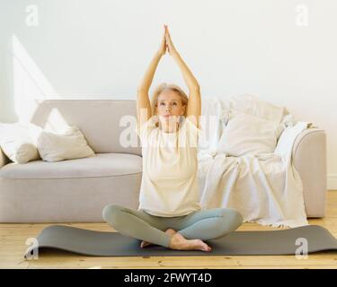 Keep calm. Peaceful focused senior woman in lotus position meditating or doing breath exercises at home, full length. Relaxed elderly female enjoying active and healthy lifestyle on retirement Stock Photo