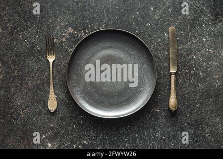 Empty vintage plate with silver knife and fork on black table.  Top view. Stock Photo