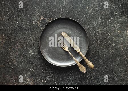 Empty vintage plate with silver knife and fork on black table.  Top view. Stock Photo