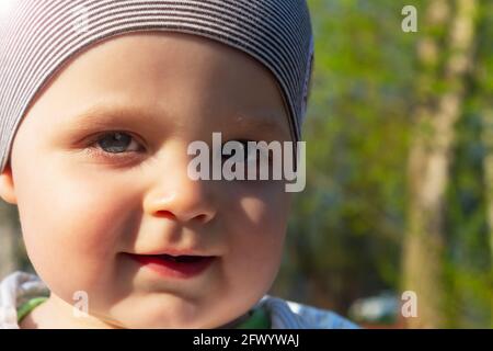 Cute caucasian baby boy in park. Close-up photo. Summer sunny day. Sun's lights falling on child face. Stock Photo