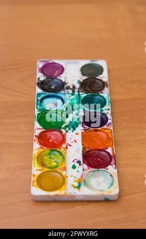 Old used set of multicolored watercolor paints for painting on the table. Top view of half-empty jars of watercolors. Flat layout on the table. Stock Photo