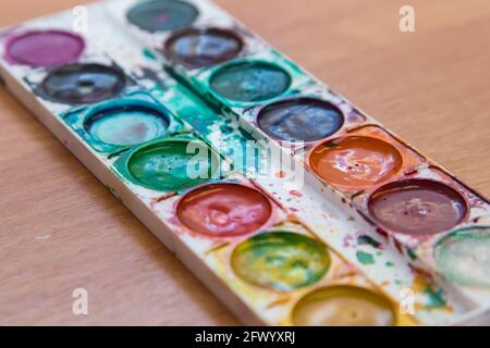 Old set of multicolored watercolor paints for painting and creativity. Top view of half-empty jars of watercolors. Flat layout on the table. Stock Photo