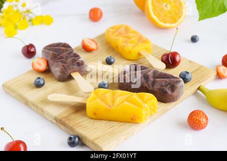 Group of homemade raspberry, cherries,strawberries, oranges, vanilla popsicles on a paddle board, frozen fruit juice, selective focus, white marble ba Stock Photo
