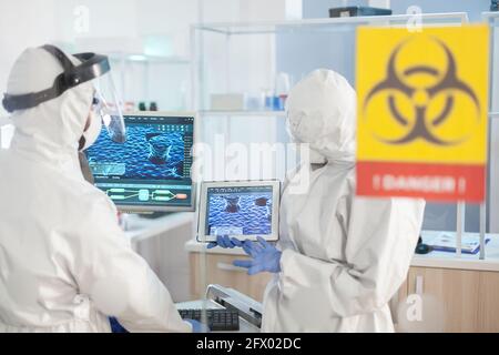 Healthcare doctors working in danger area of lab dressed in ppe suit during global pandemic. Group of doctors examining vaccine evolution using high tech for diagnosis against covid19. Stock Photo