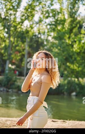 Happy young beautiful afro american woman smiling and using mobile phone. Green background. Spring or summer season. Casual clothing outdoors. High quality photo Stock Photo